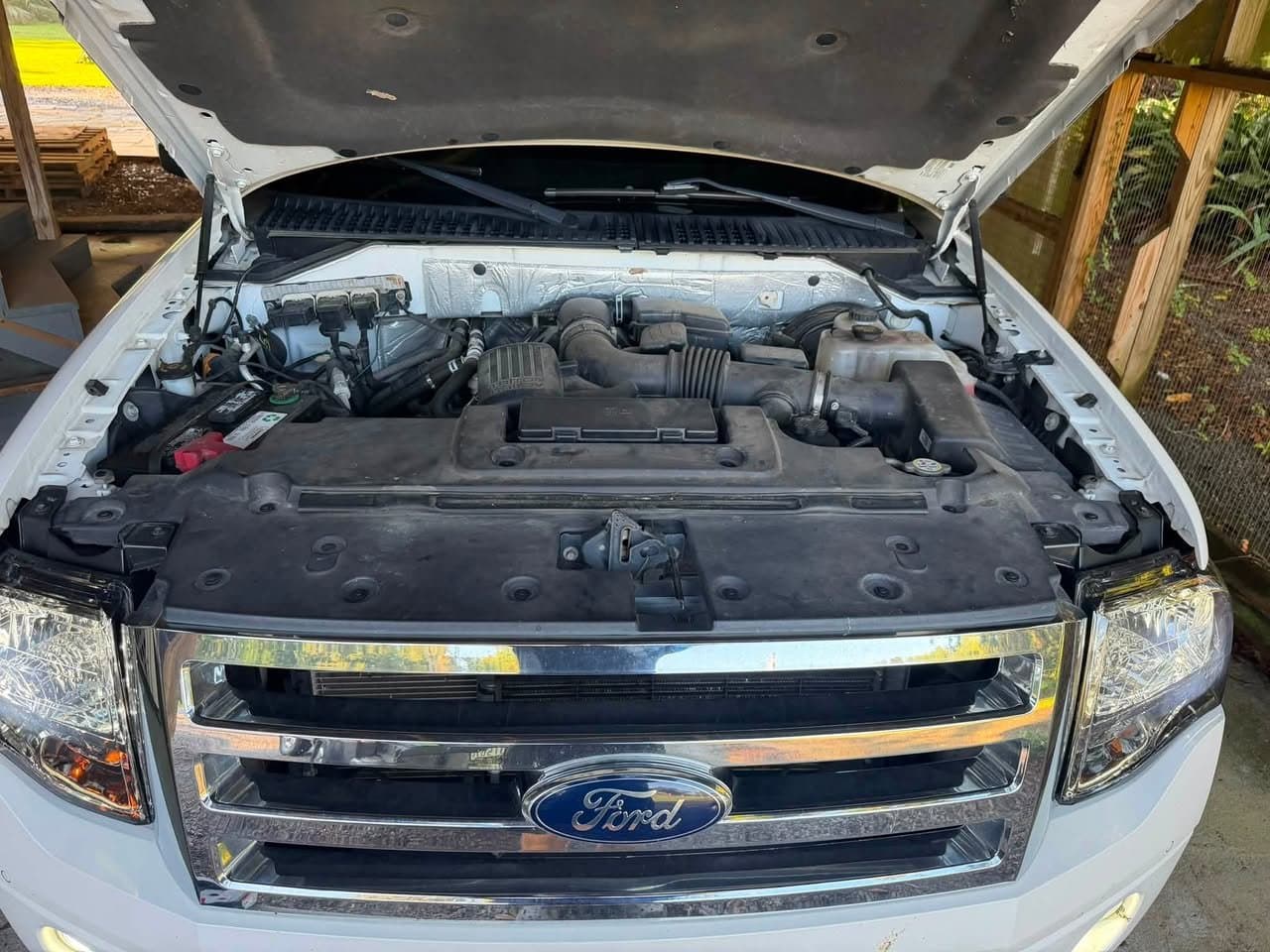 A Ford Expedition engine bay before service, with a grey film of dust across the radiator cover and engine cover