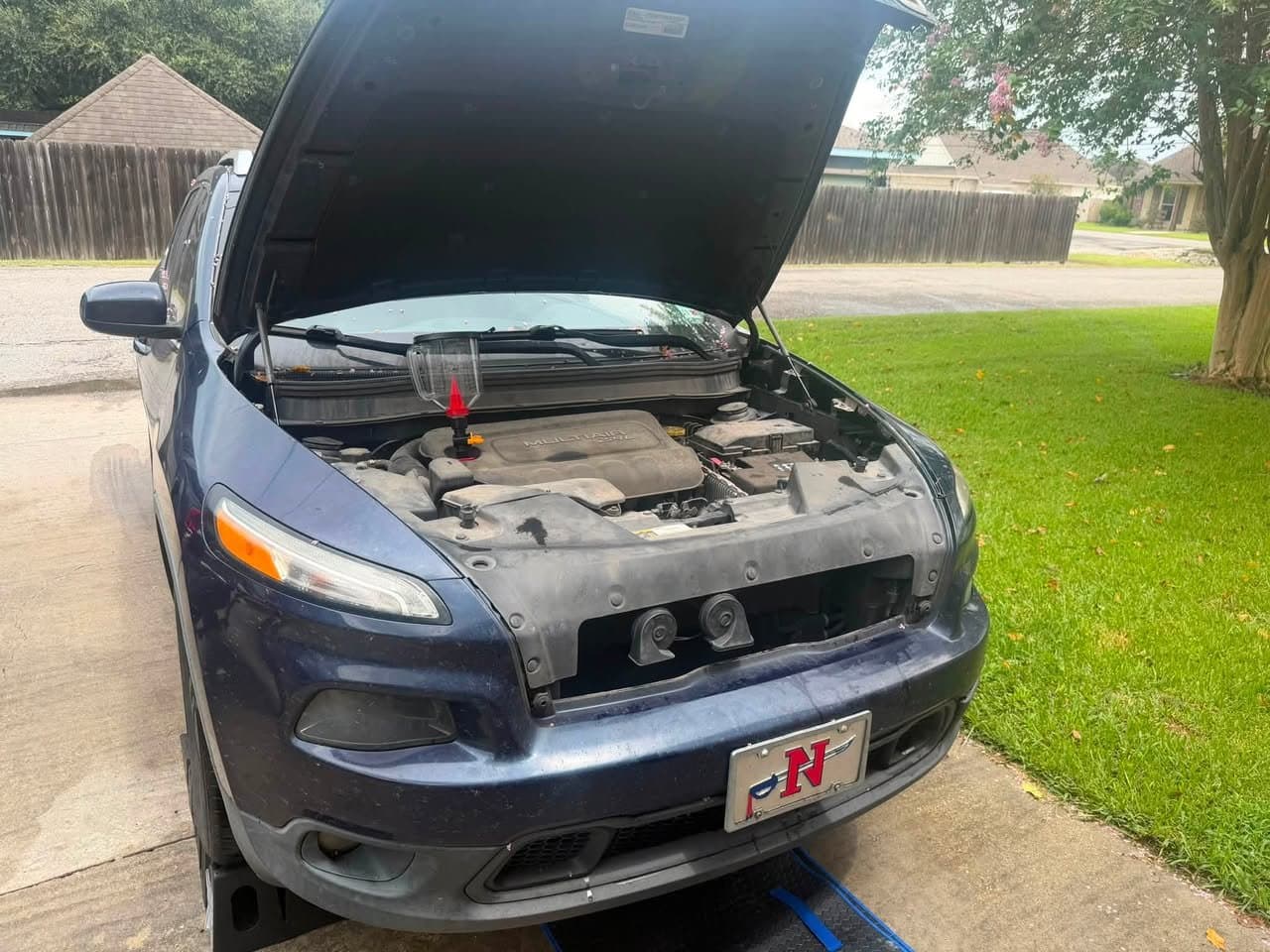 A Jeep Cherokee engine bay before service, with dust dulling the engine cover and radiator shroud