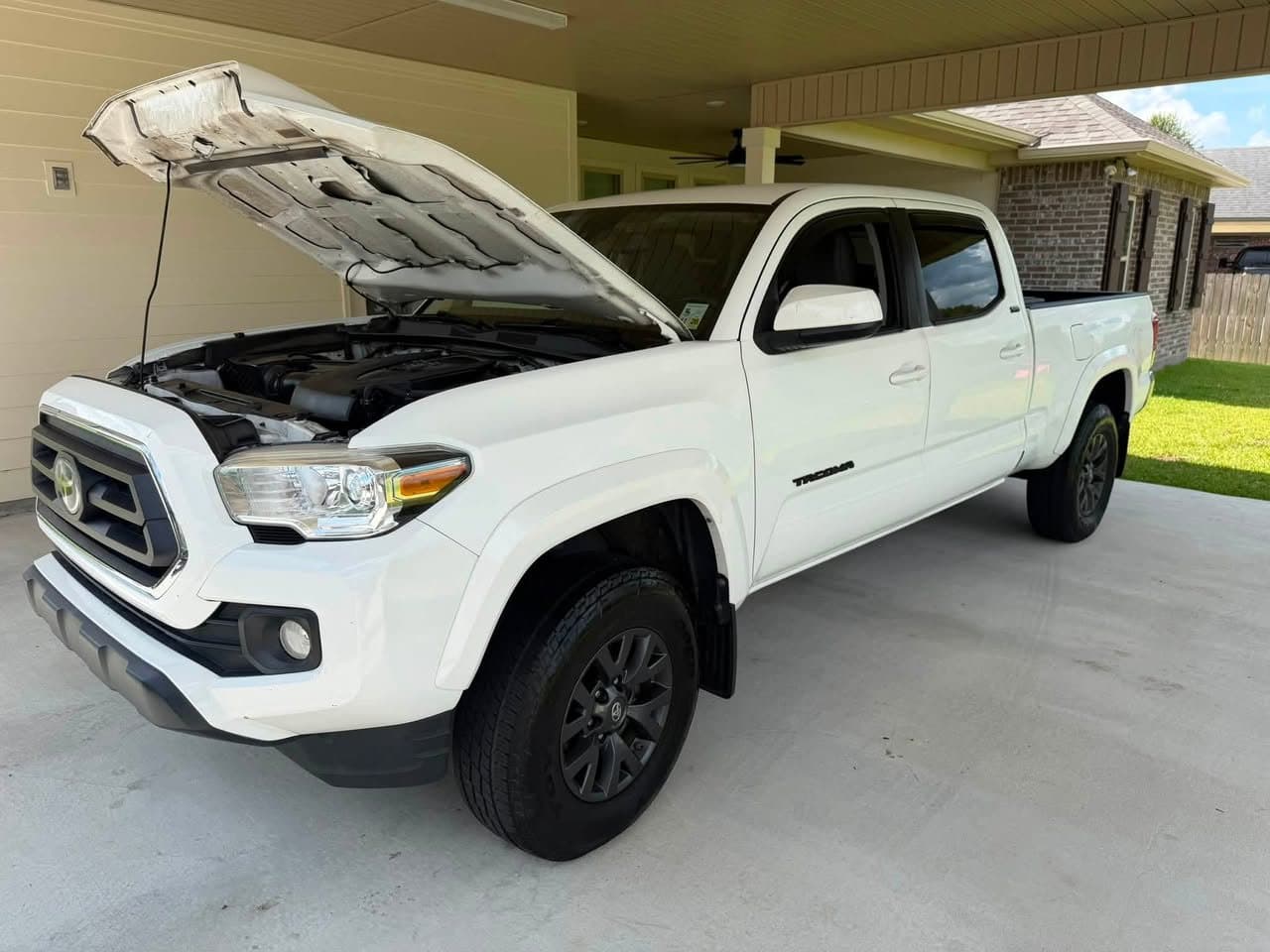 A white Toyota Tacoma with the hood up under a carport being serviced at home