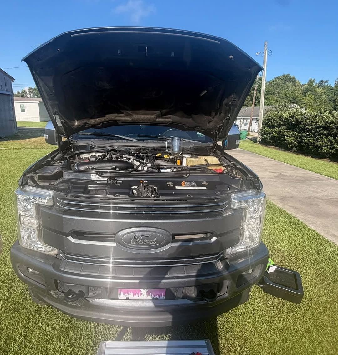 A Ford SUV with the hood up in a yard in the late afternoon during a service call